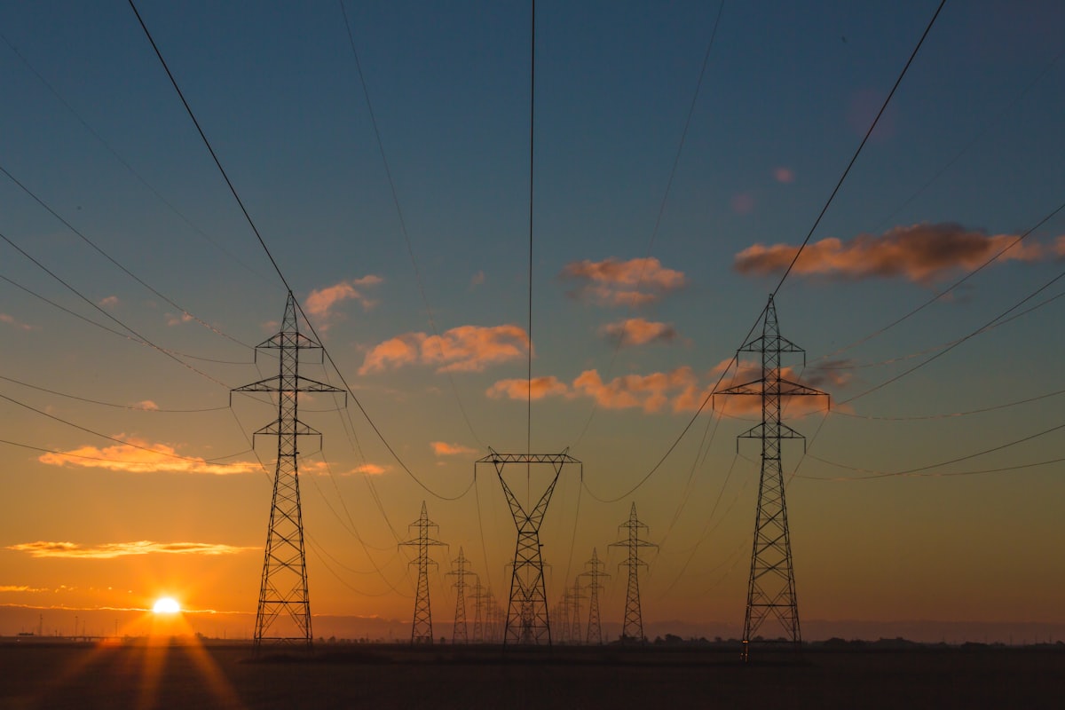 Electricity transmission pylons and power lines silhouetted against a sunset sky