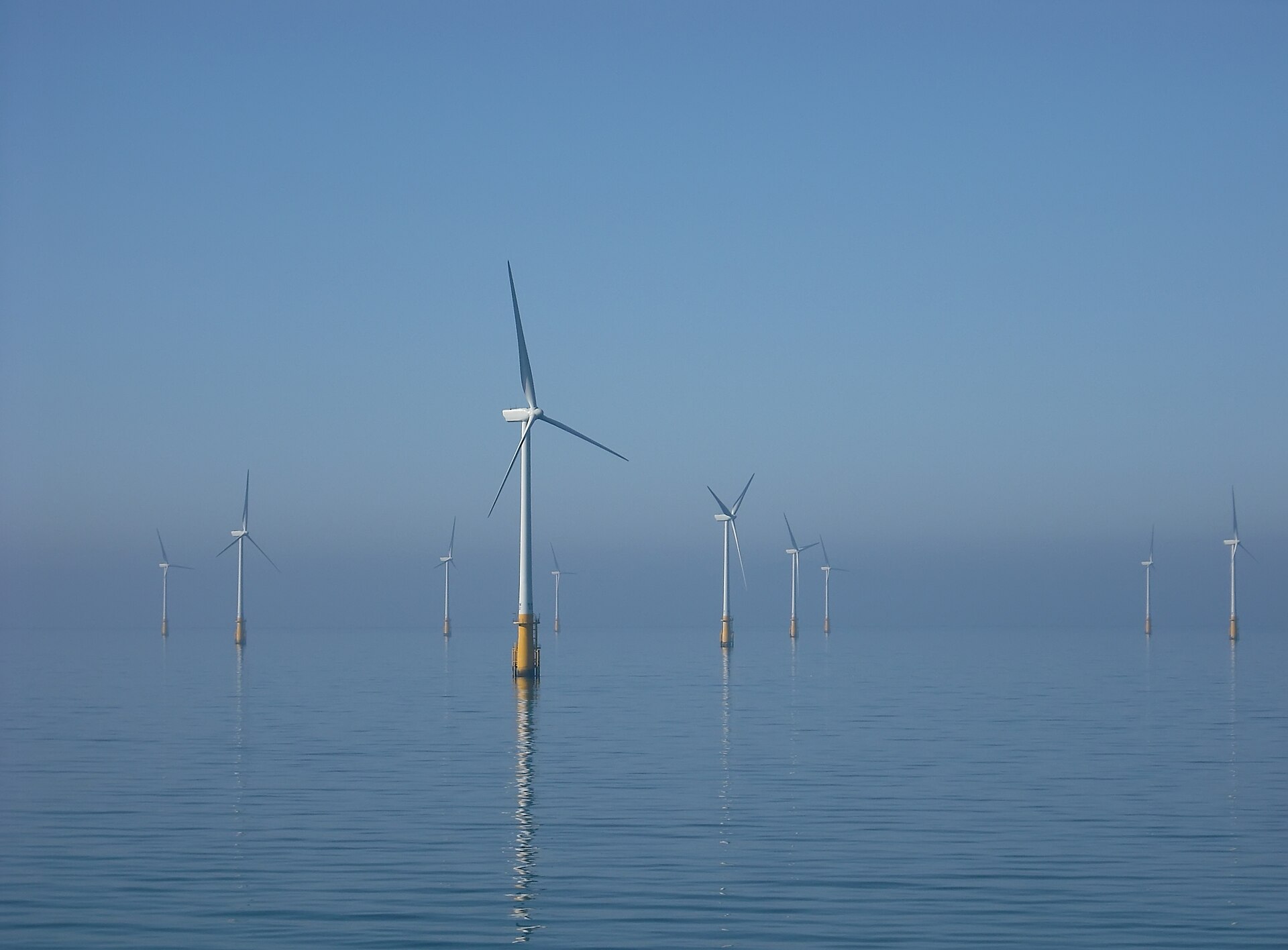 A group of offshore wind turbines rising from calm sea on a misty morning